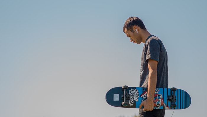 Man holding a skateboard against a blue sky