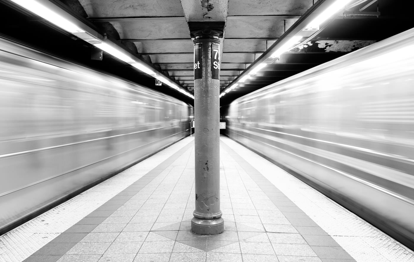 NYC Subway trains rushing by on both sides of platform, creating blurred space around the centre